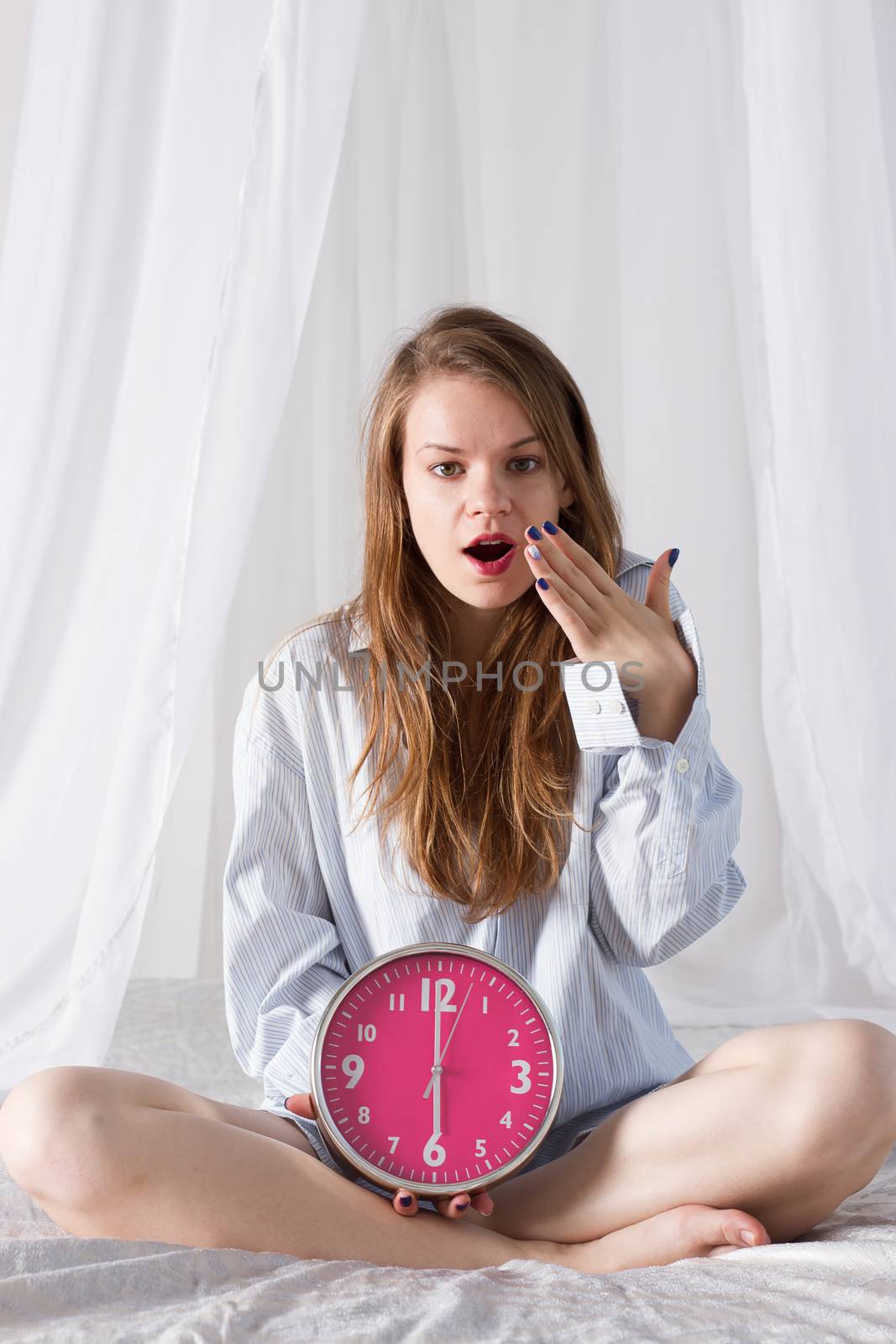 girl is sitting on the bed with big pink clock. 6 a.m