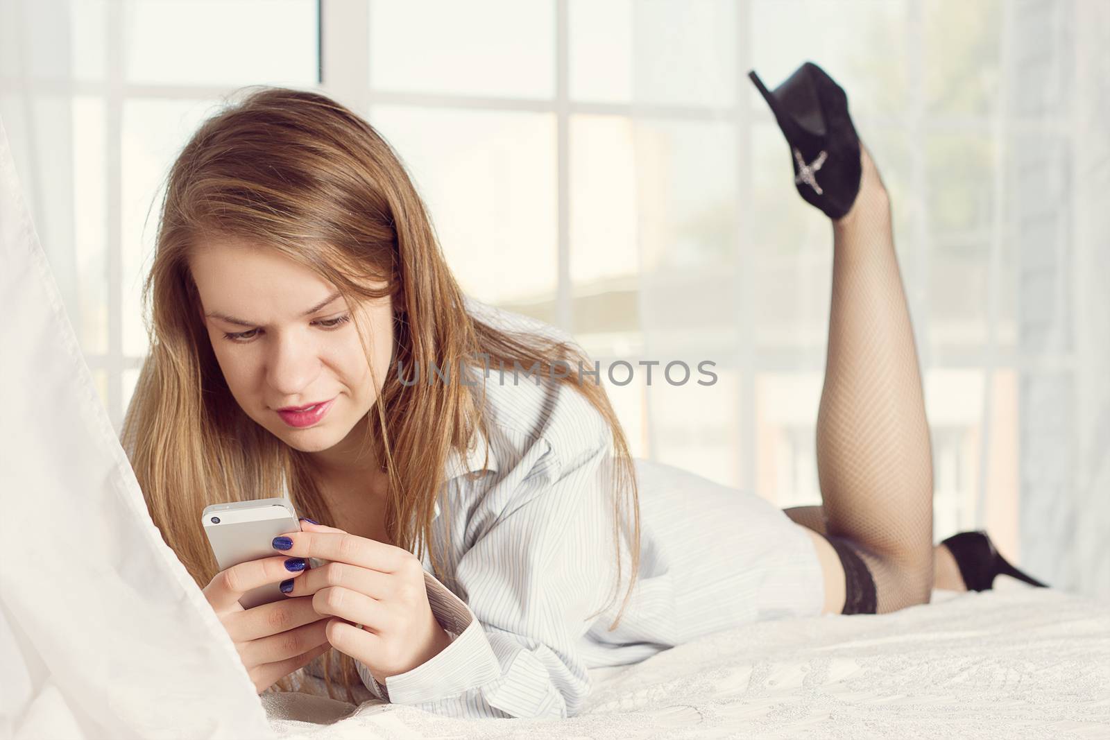 girl lies in a man's shirt on the bed with a smartphone in the hands of