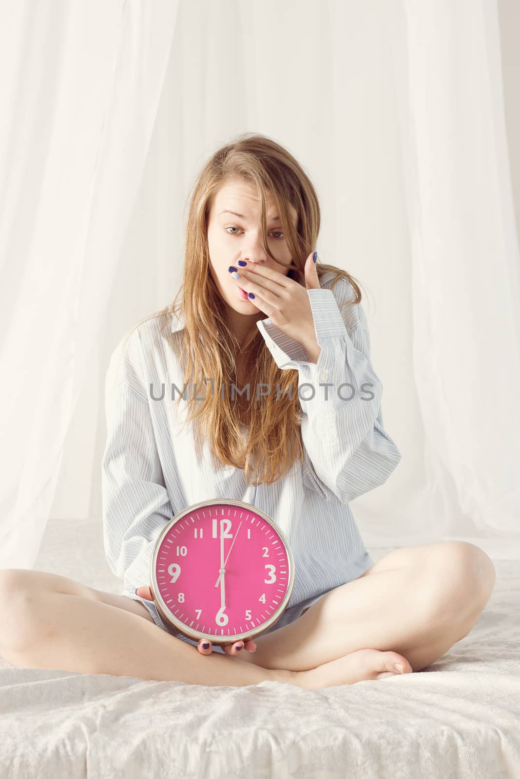 girl is sitting on the bed with big pink clock. 6 a.m