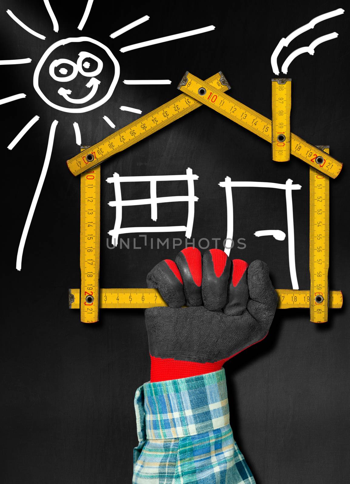 Hand holding a wooden meter ruler in the shape of house with sun, door, window and smoke from the chimney. On a blackboard. Concept of house project