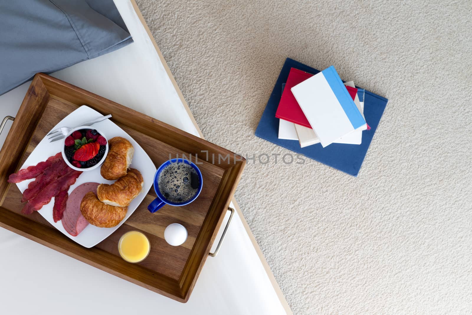 High Angle View of Stack of Books on Floor Beside Bed with Breakfast in Bed Tray on Top with Assortment of Food