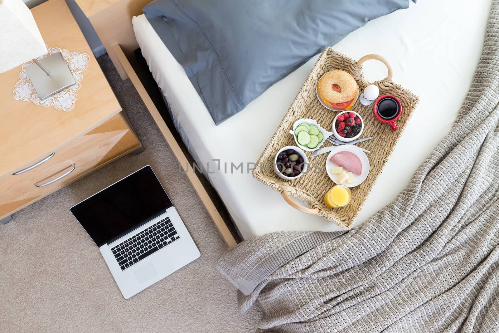 High Angle View of Open Laptop on Floor Beside Unmade Bed in Hotel Room with Wicker Breakfast Tray