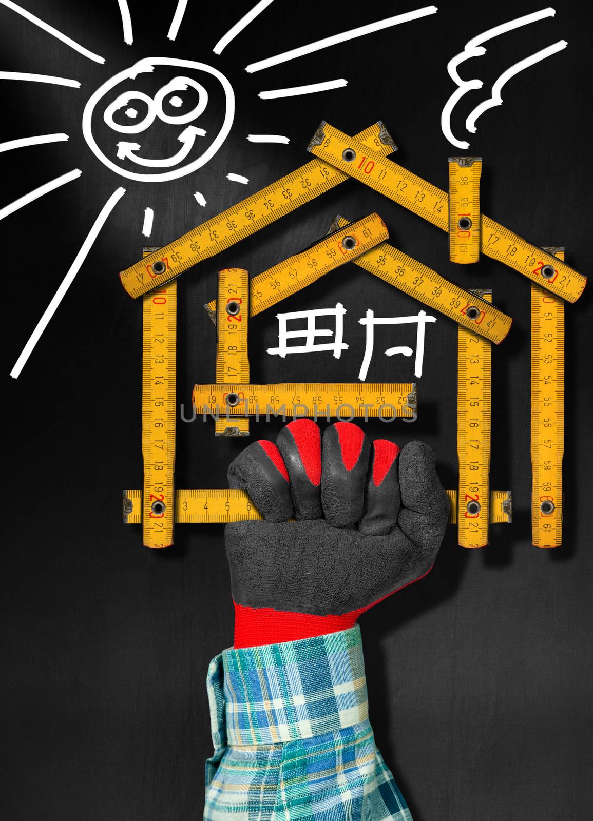 Hand holding a wooden meter ruler in the shape of house with sun, door, window and smoke from the chimney. On a blackboard. Concept of house project 
