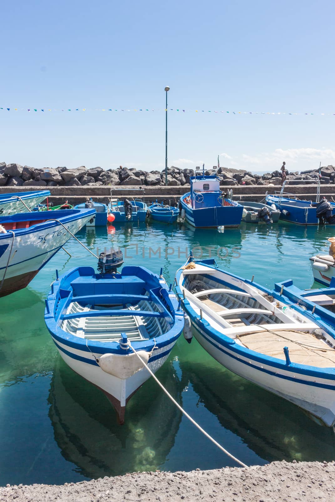 Several small colorful boats are anchored in the harbor of Catania, SIcily-Italy on the coast of the Mediterranean Sea.