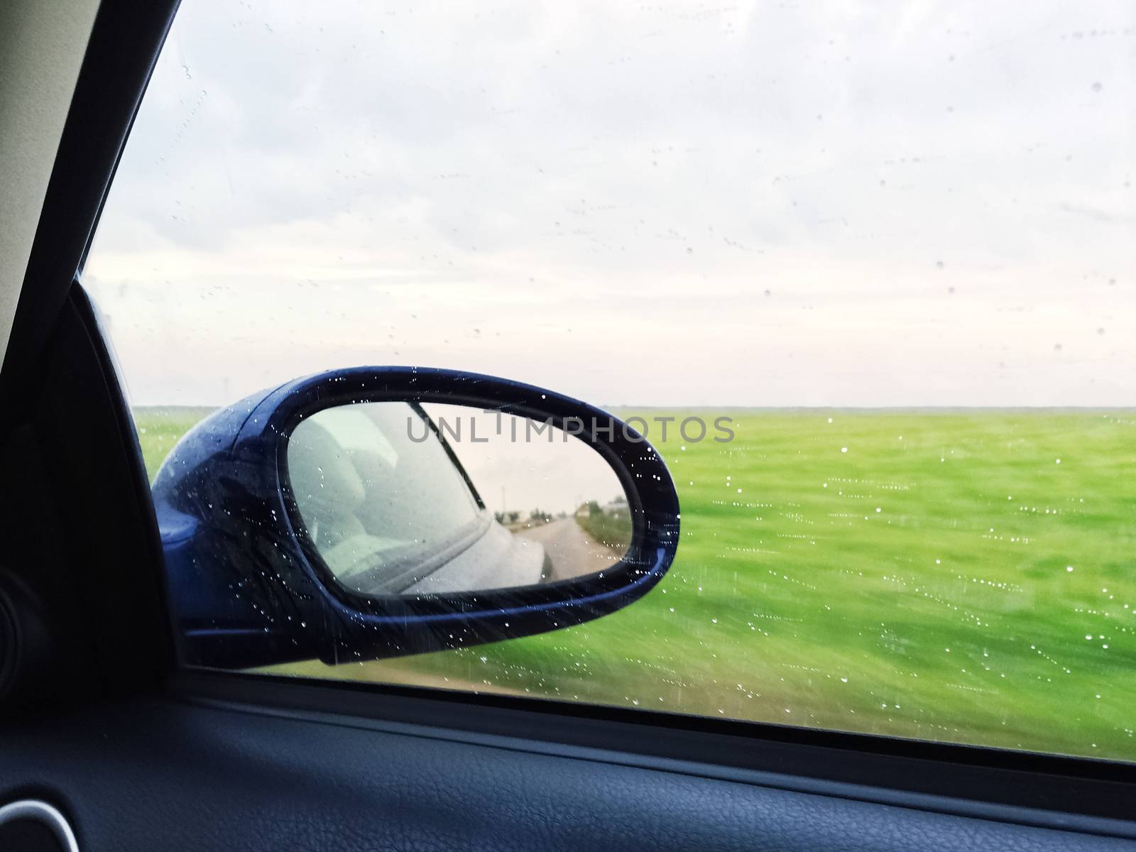 View over green fields from a modern car, raindrops on the window.