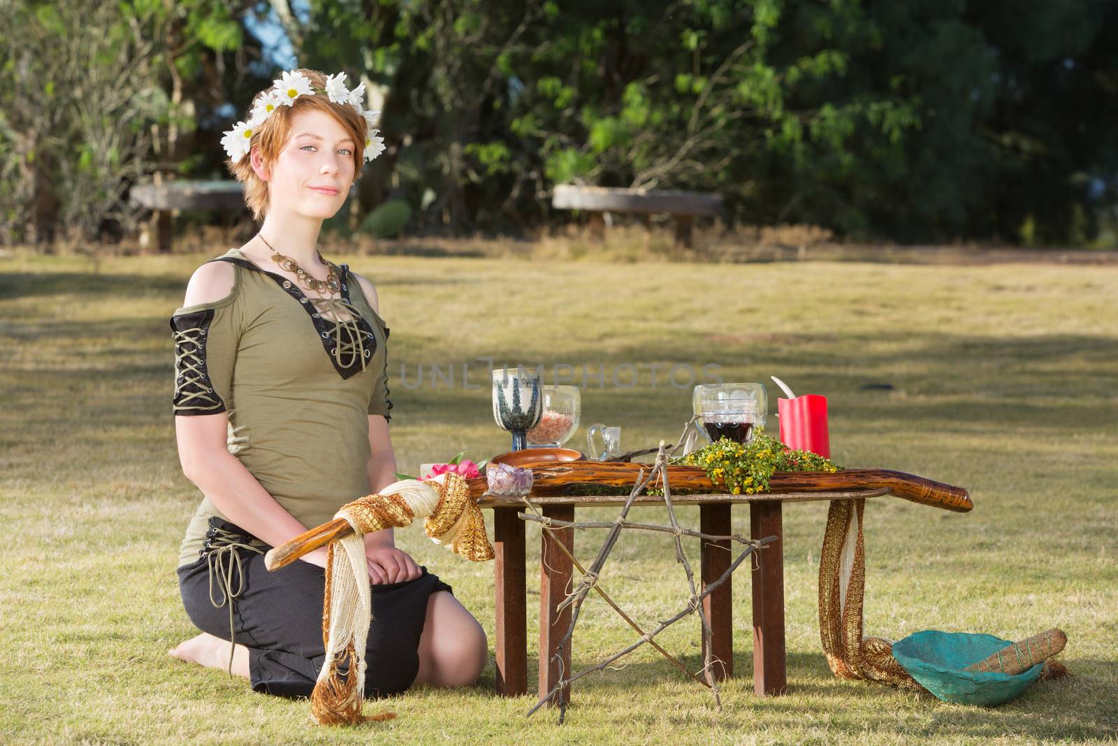 Cute pagan woman with wreath sitting at outdoor altar