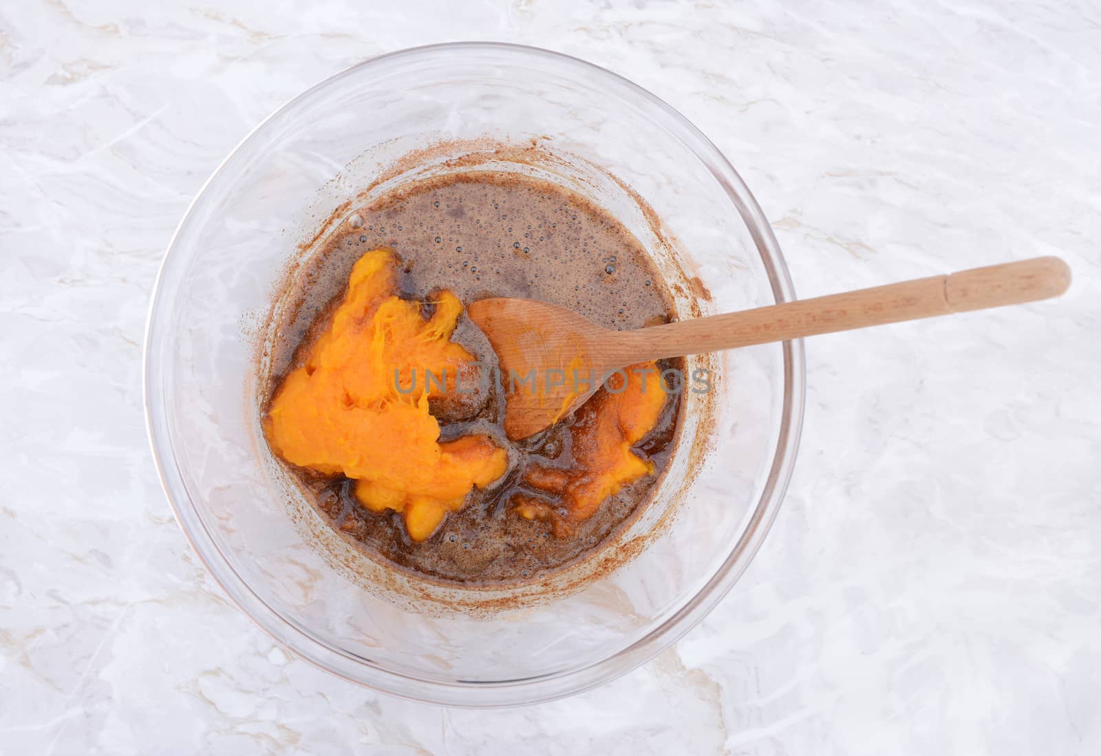 Stirring pureed pumpkin into pie filling in a glass bowl with a wooden spoon 