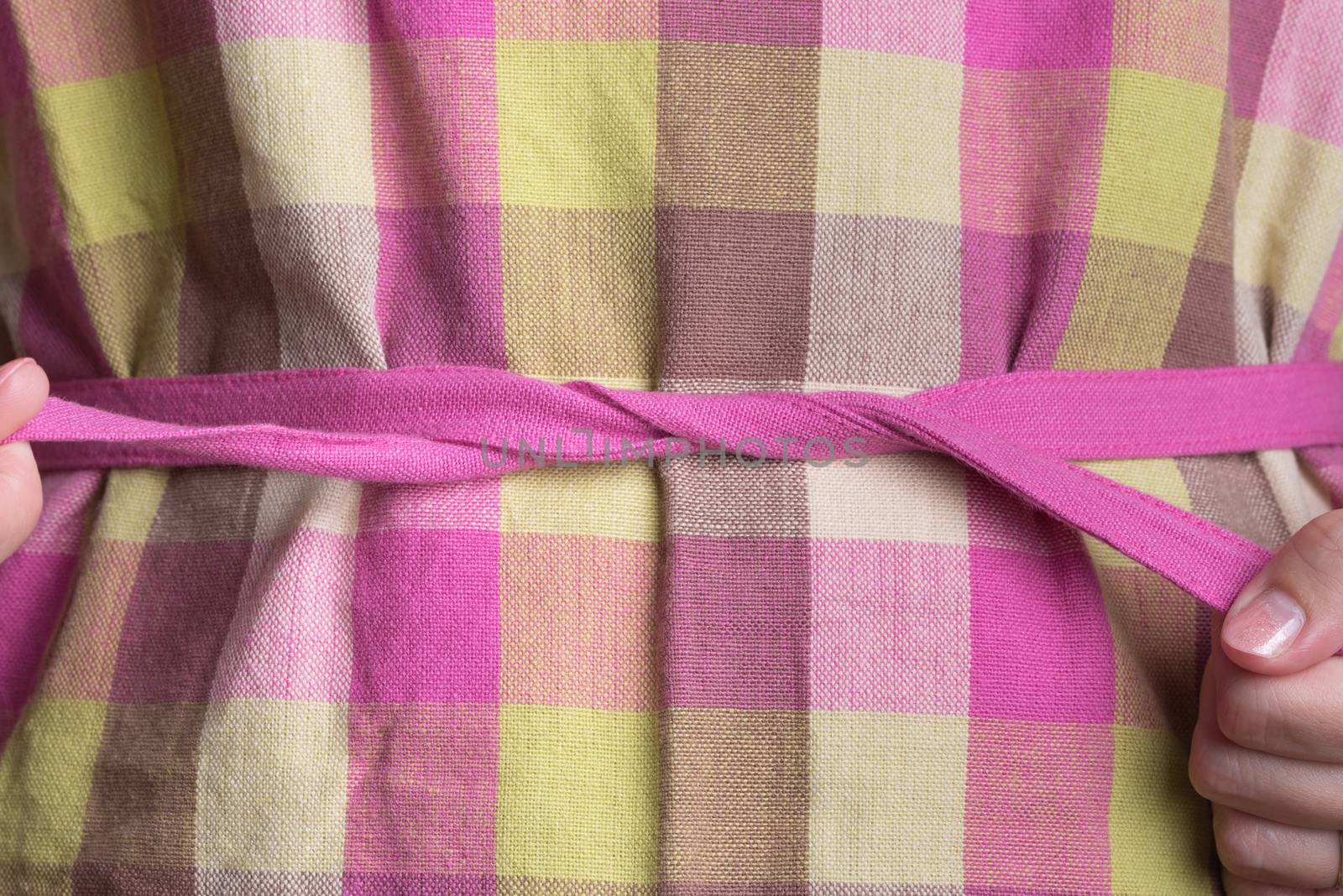 A woman tying a pink and yellow plaid apron.