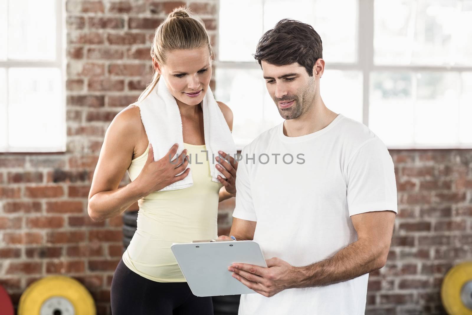 Woman discussing her performance on clipboard with trainer in crossfit gym