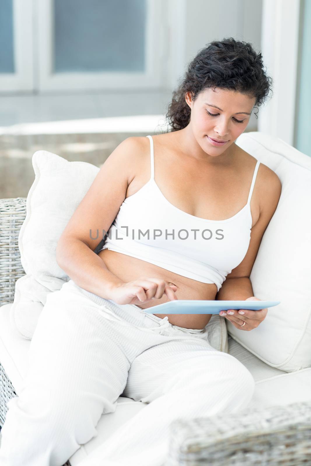 Pregnant woman using tablet pc of sofa at home