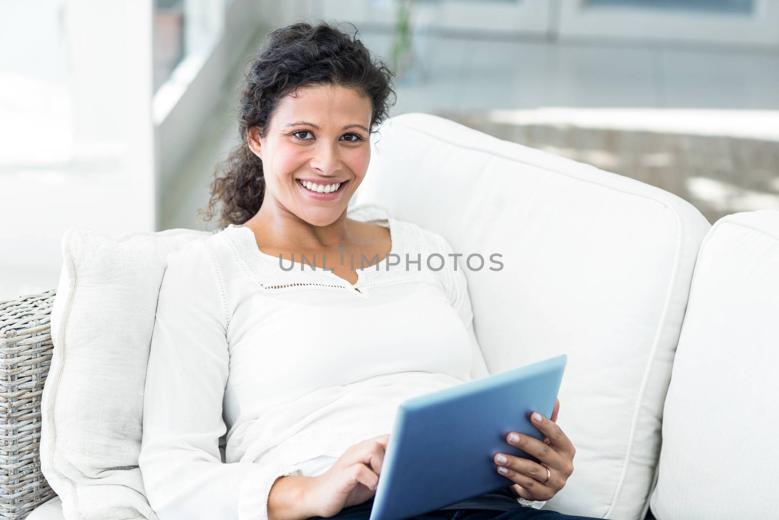 Portrait of happy pregnant woman sitting with tablet on sofa at home
