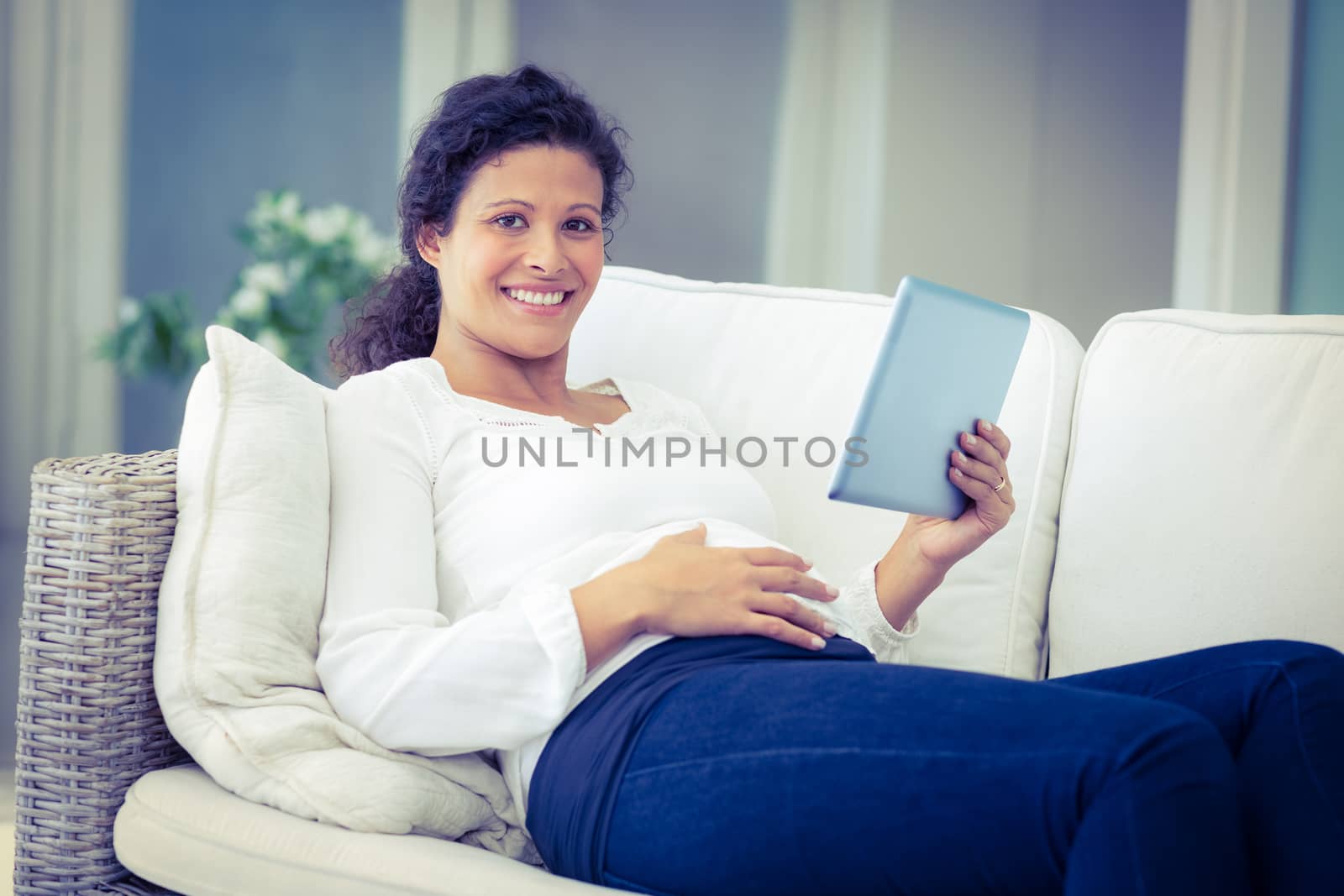 Portrait of happy pregnant woman reclining on sofa with tablet at home