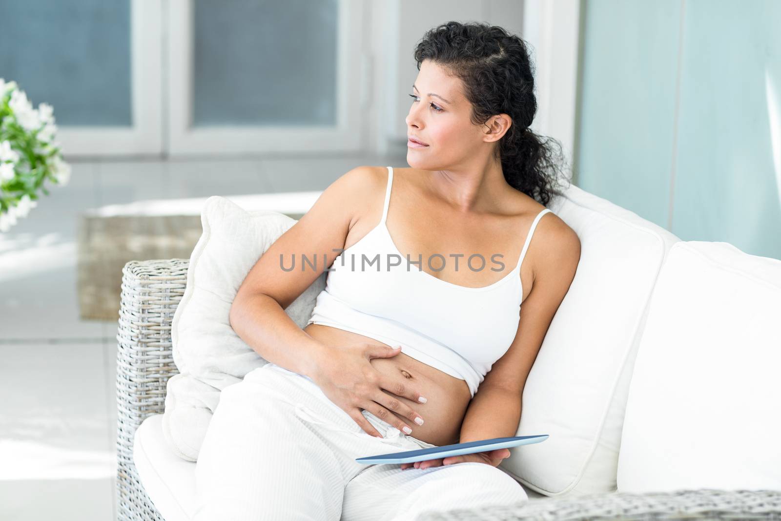 Happy pregnant woman sitting on sofa with tablet in living room