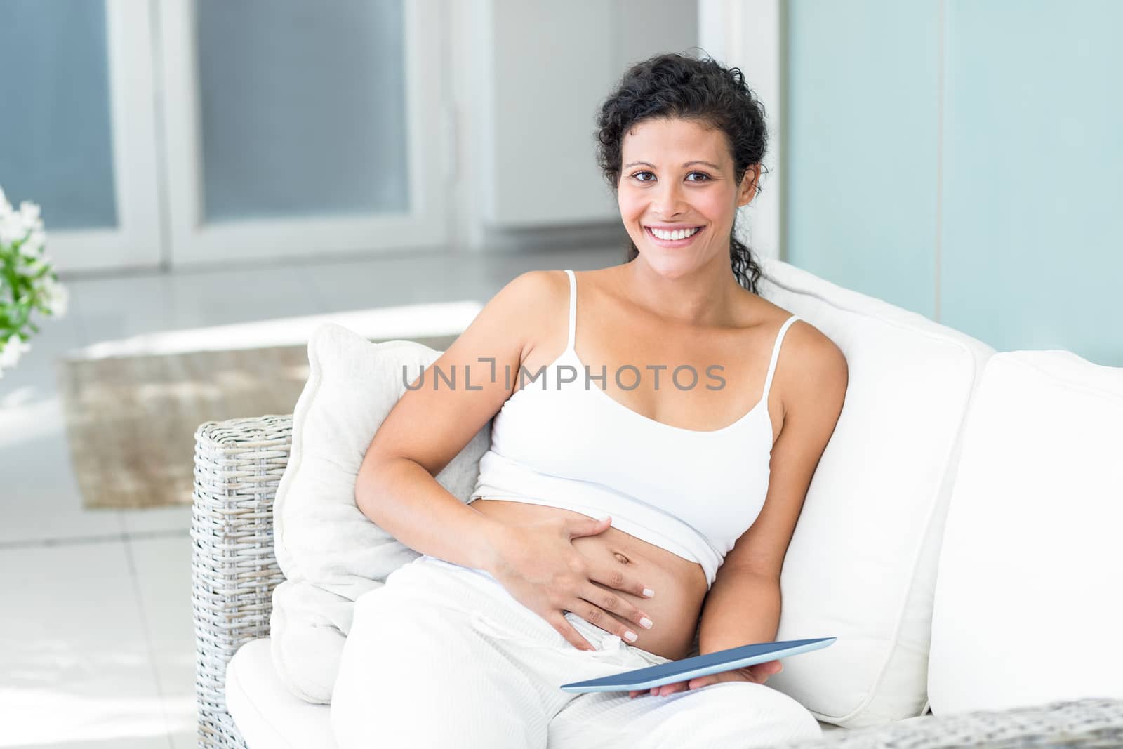 Portrait of happy pregnant woman sitting on sofa with tablet in living room