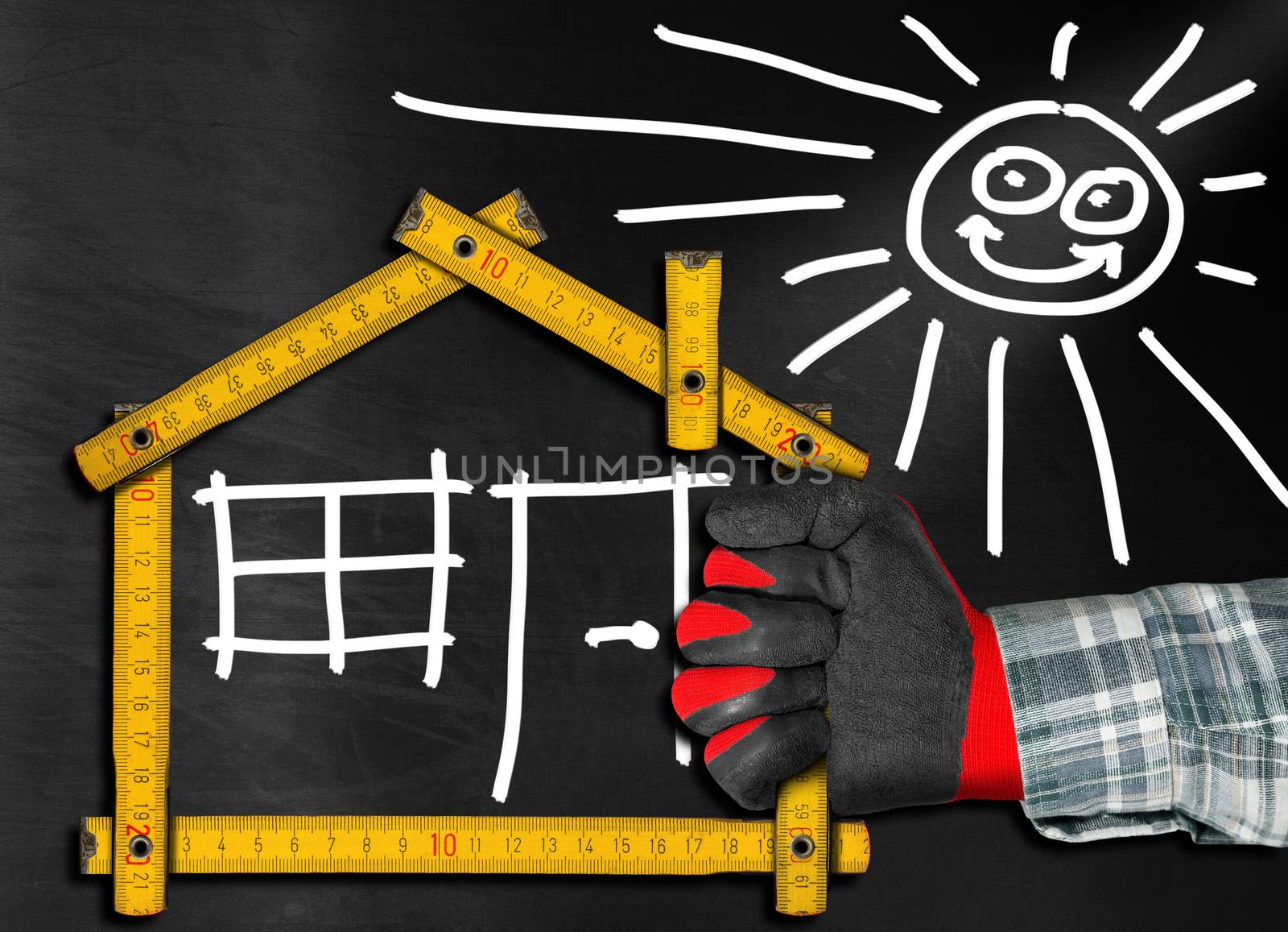 Hand holding a wooden meter ruler in the shape of house with sun, door, window and smoke from the chimney. On a blackboard. Concept of house project 