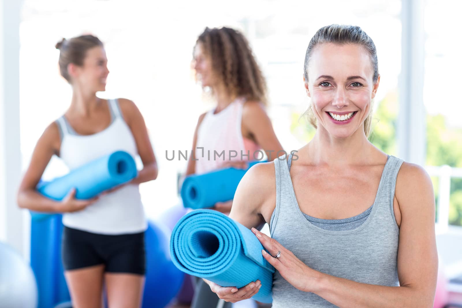 Portrait of woman holding yoga mat in fitness studio