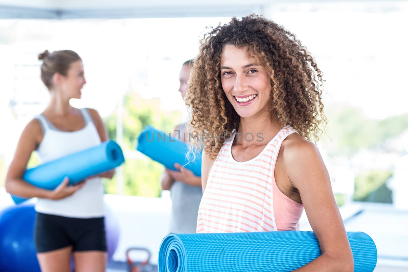 Portrait of smiling woman holding yoga mat in fitness studio