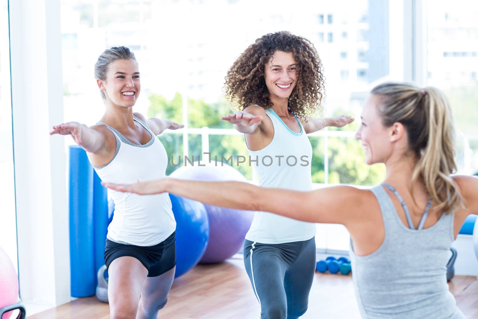 Smiling women doing warrior II pose in fitness studio