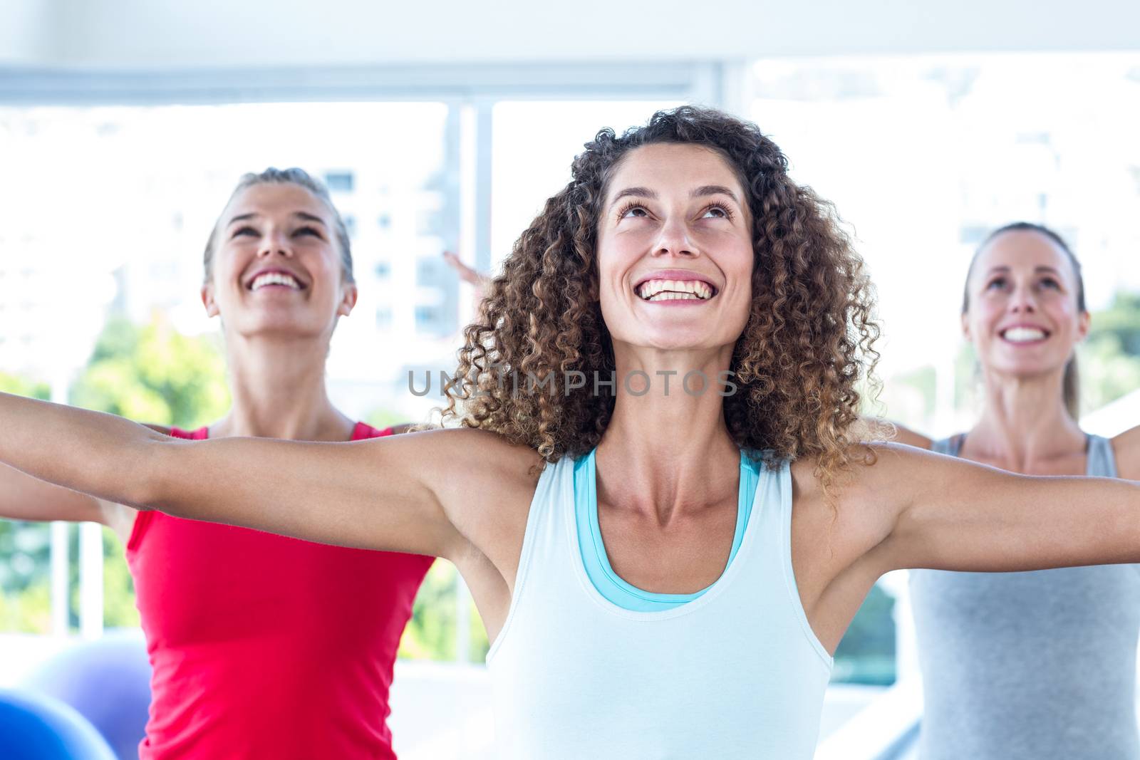 Fit women looking up and smiling with arms outstretched in fitness studio