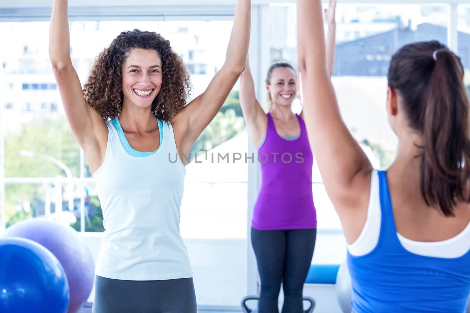 Cropped image of cheerful and fit women with arms raised in fitness studio
