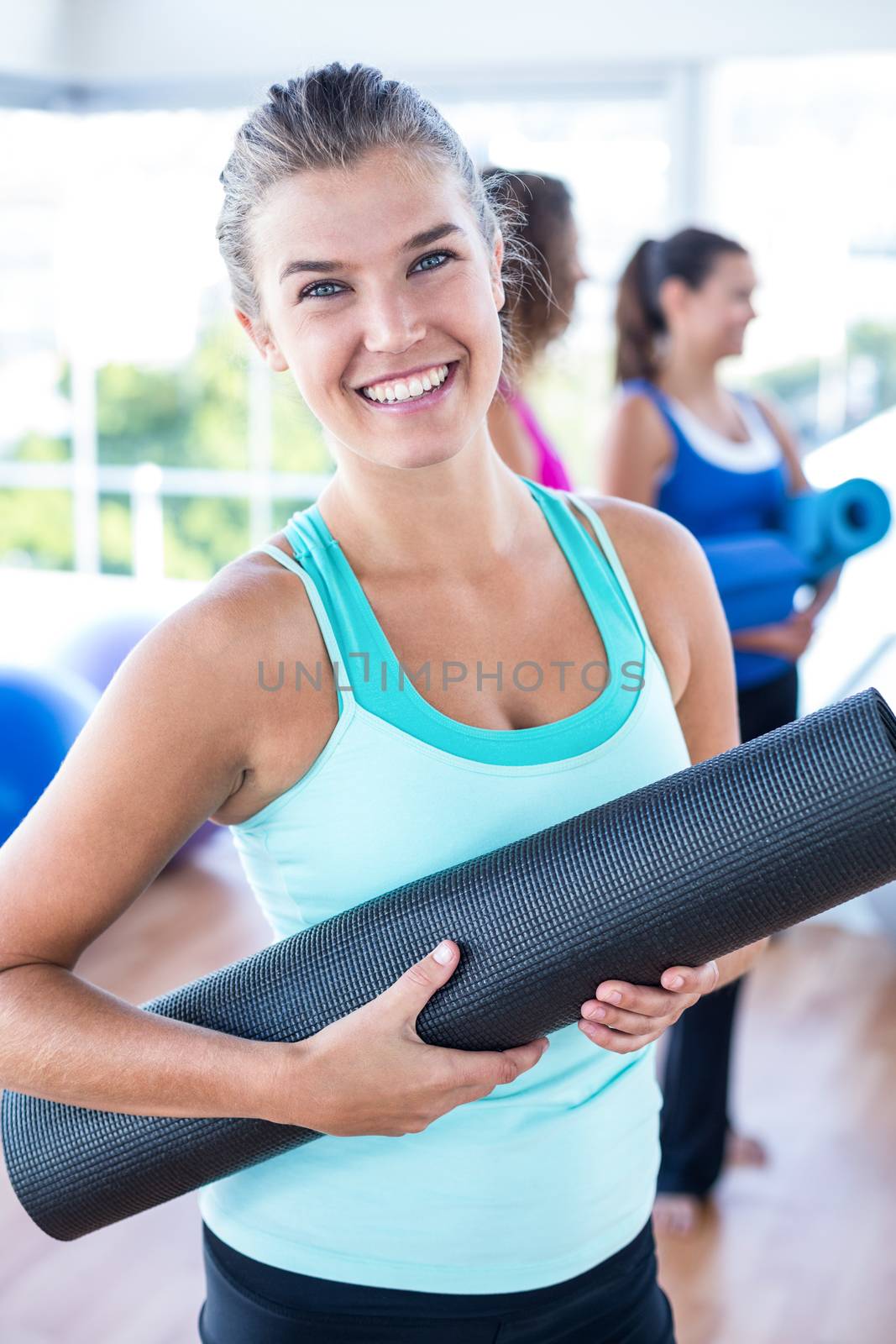 Portrait of beautiful woman smiling while holding exercise mat in fitness studio
