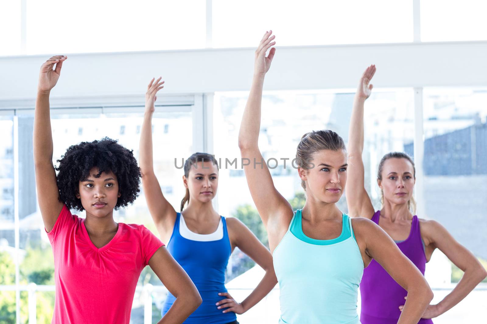 Focused woman in fitness studio with left arm raised while standing