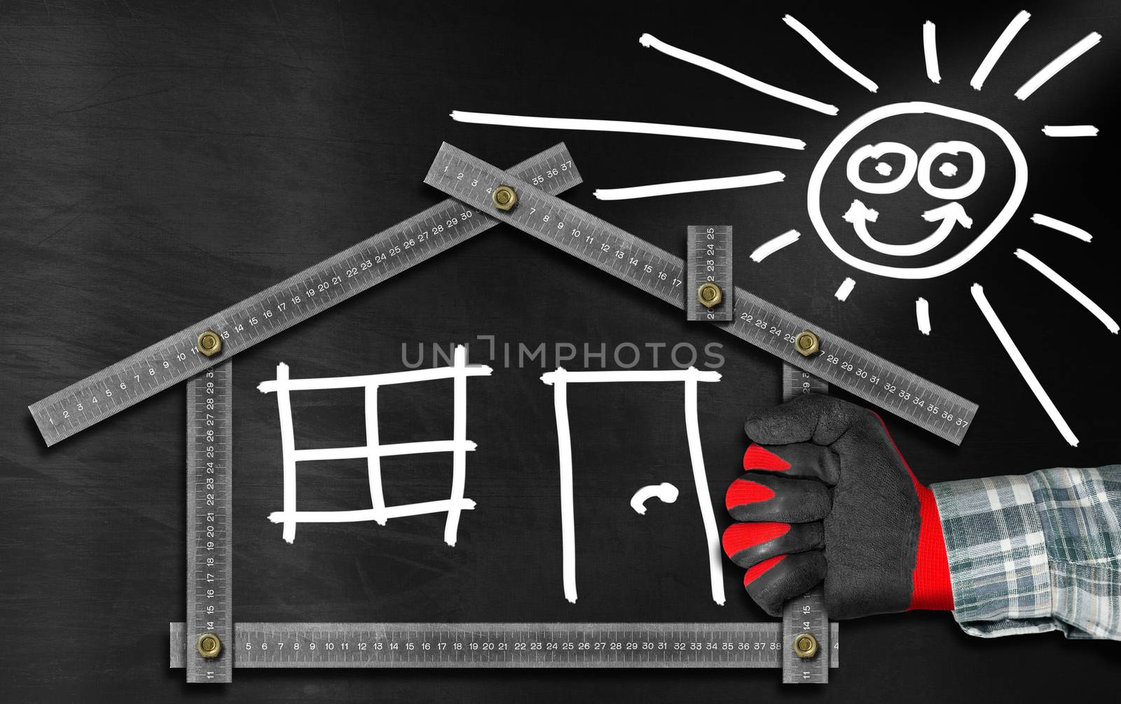 Hand holding a metal meter ruler in the shape of house with sun, door, window and smoke from the chimney. On a blackboard. Concept of house project 