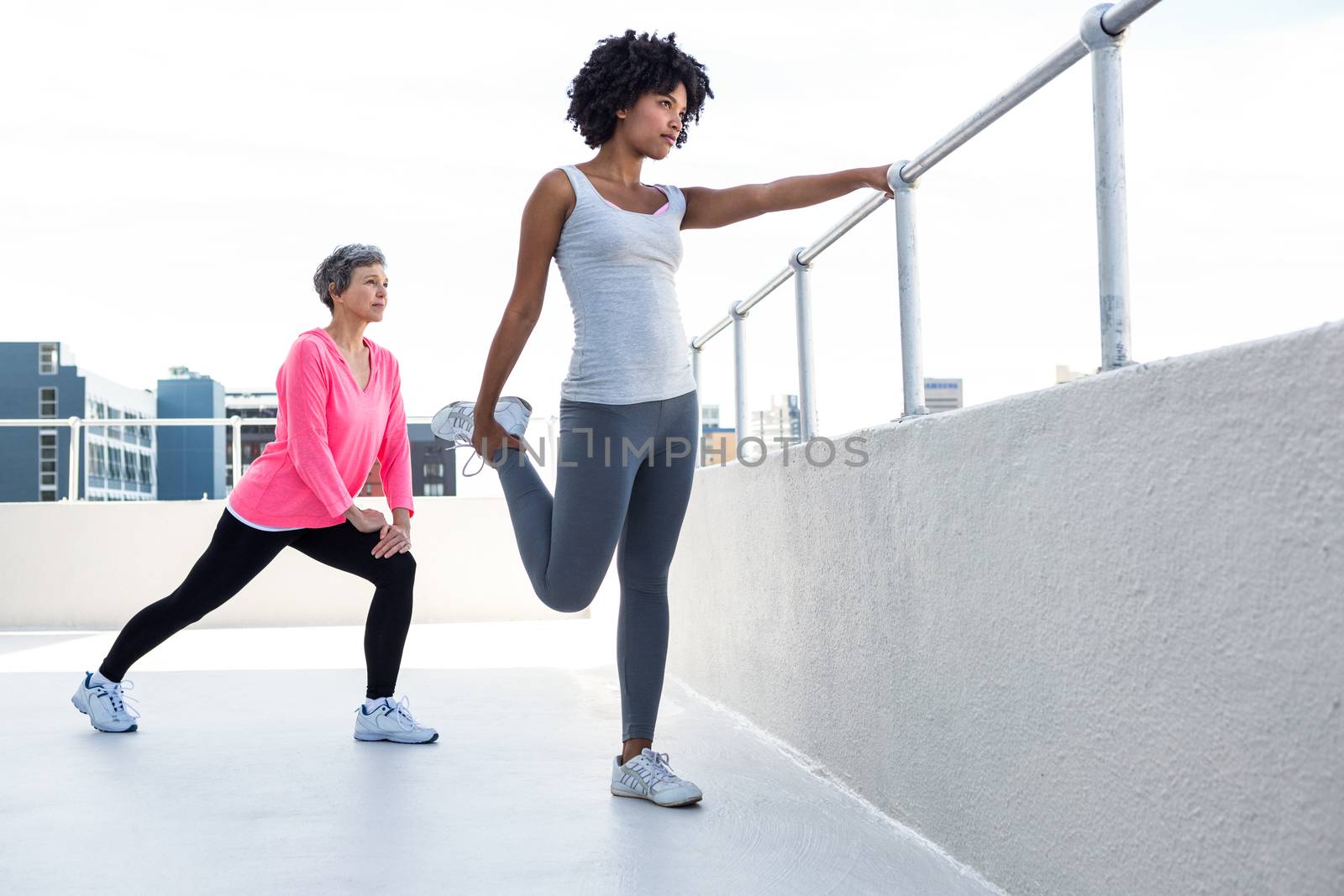 Woman exercising with female friend by railing outdoors