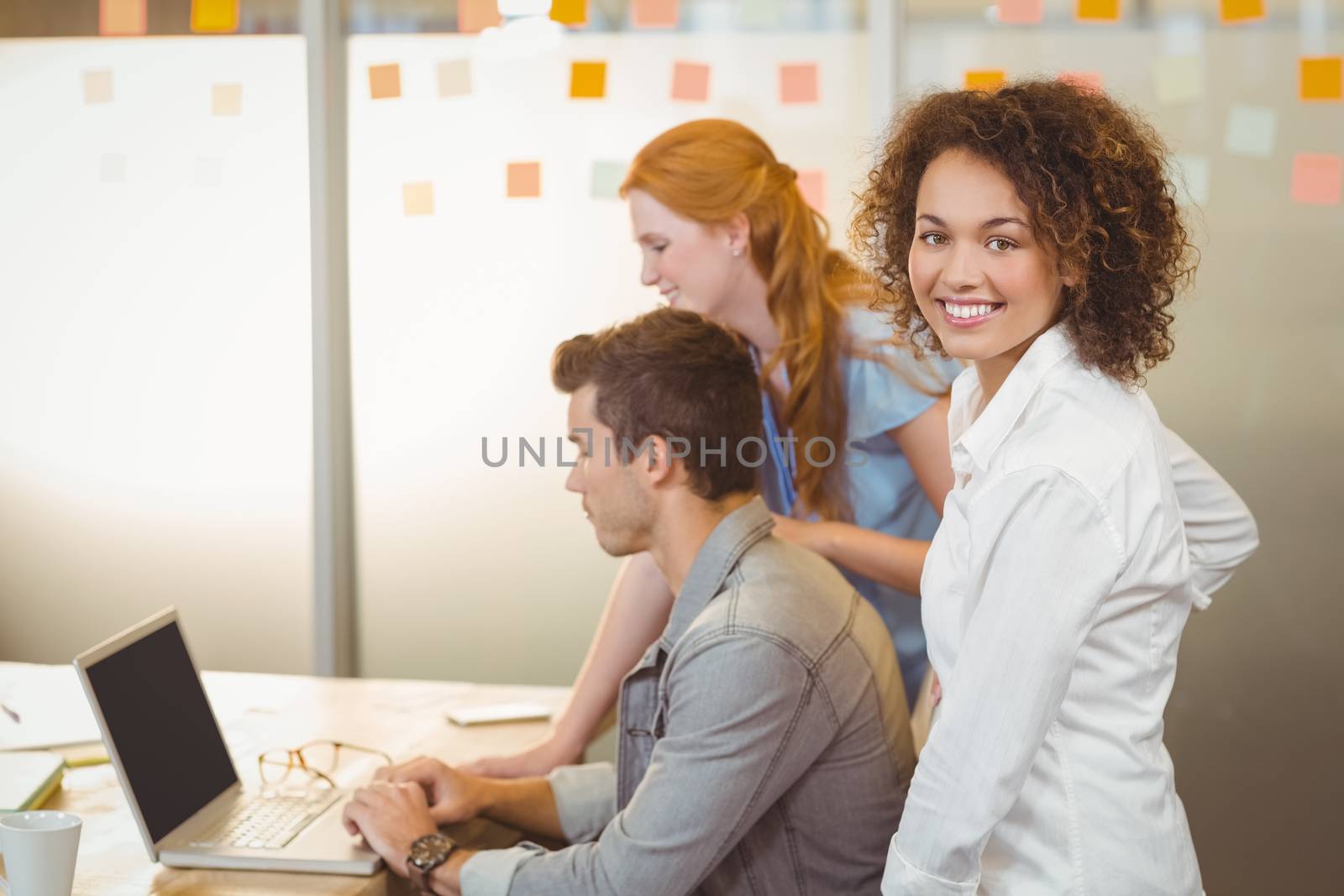 Portrait of businesswoman with colleagues using laptop at work in office
