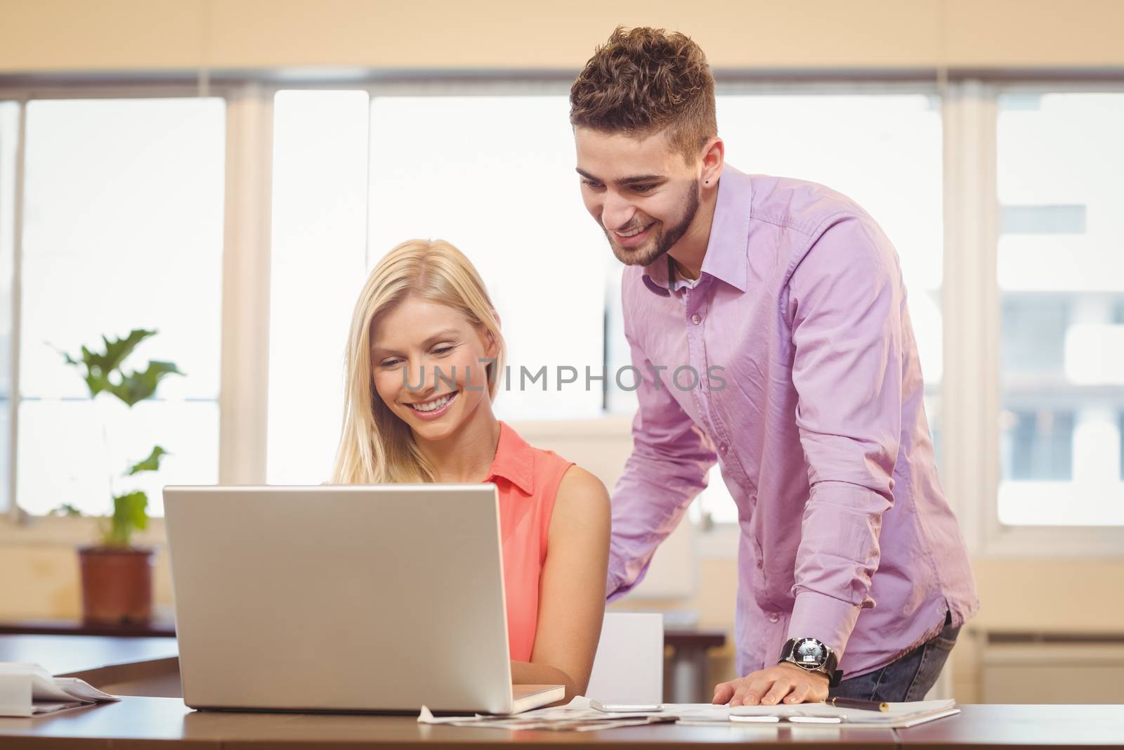 Happy business people looking at laptop in creative office