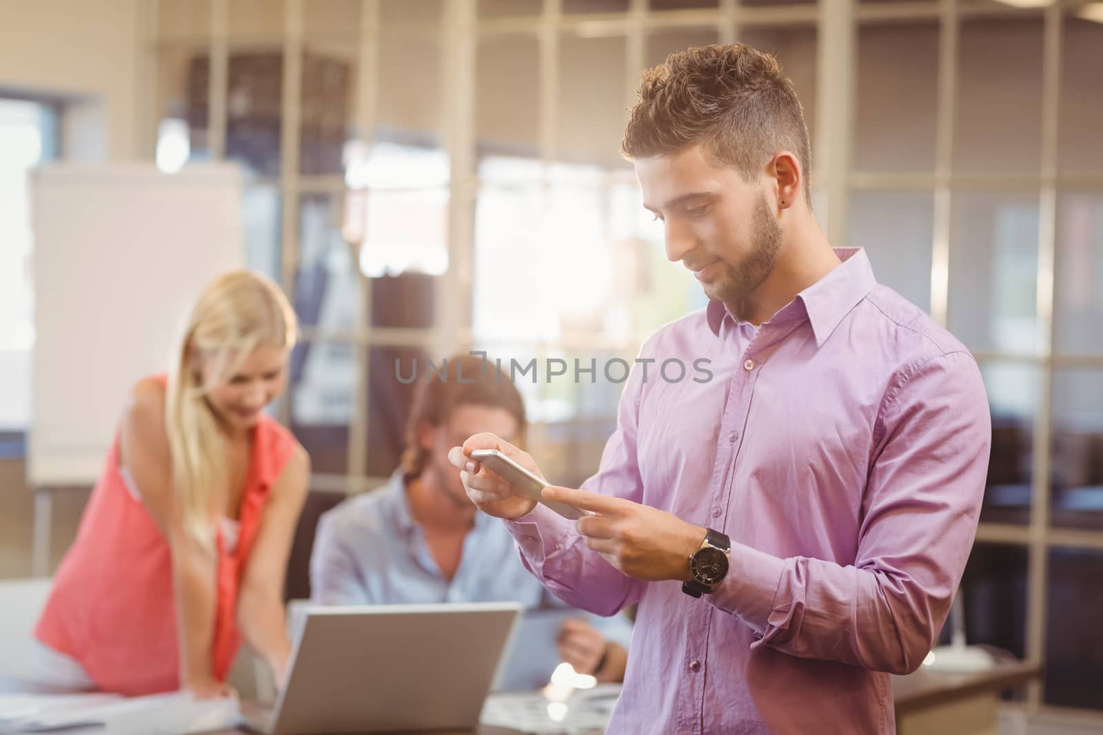 Businessman using phone in office with colleagues working in background