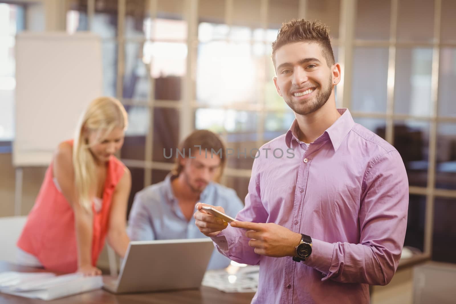 Portrait of businessman using phone in office with colleagues working in background