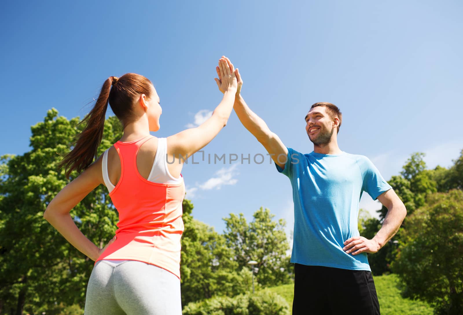 two smiling people making high five outdoors by dolgachov