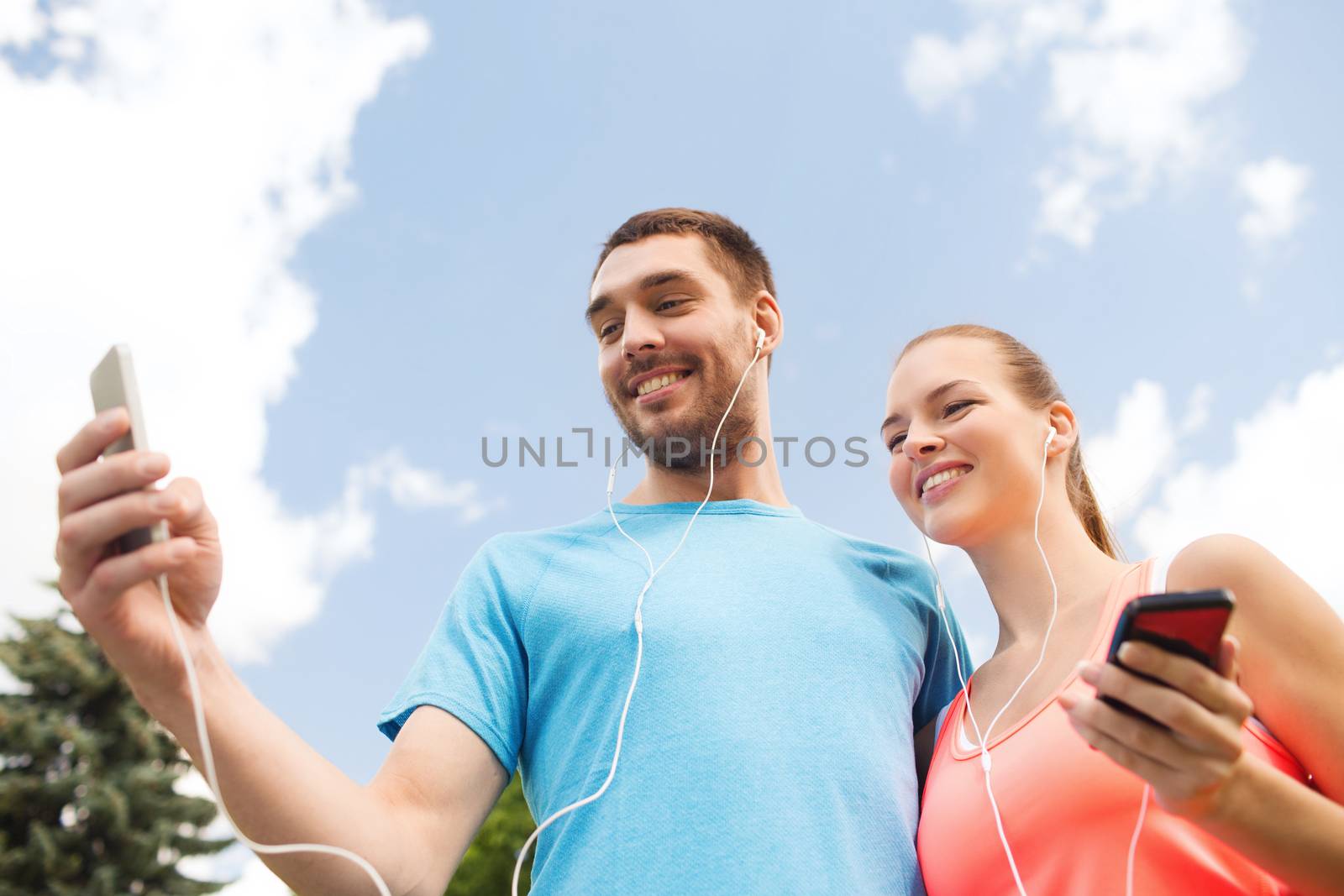 fitness, sport, training, technology and lifestyle concept - two smiling people with smartphones and earphones outdoors