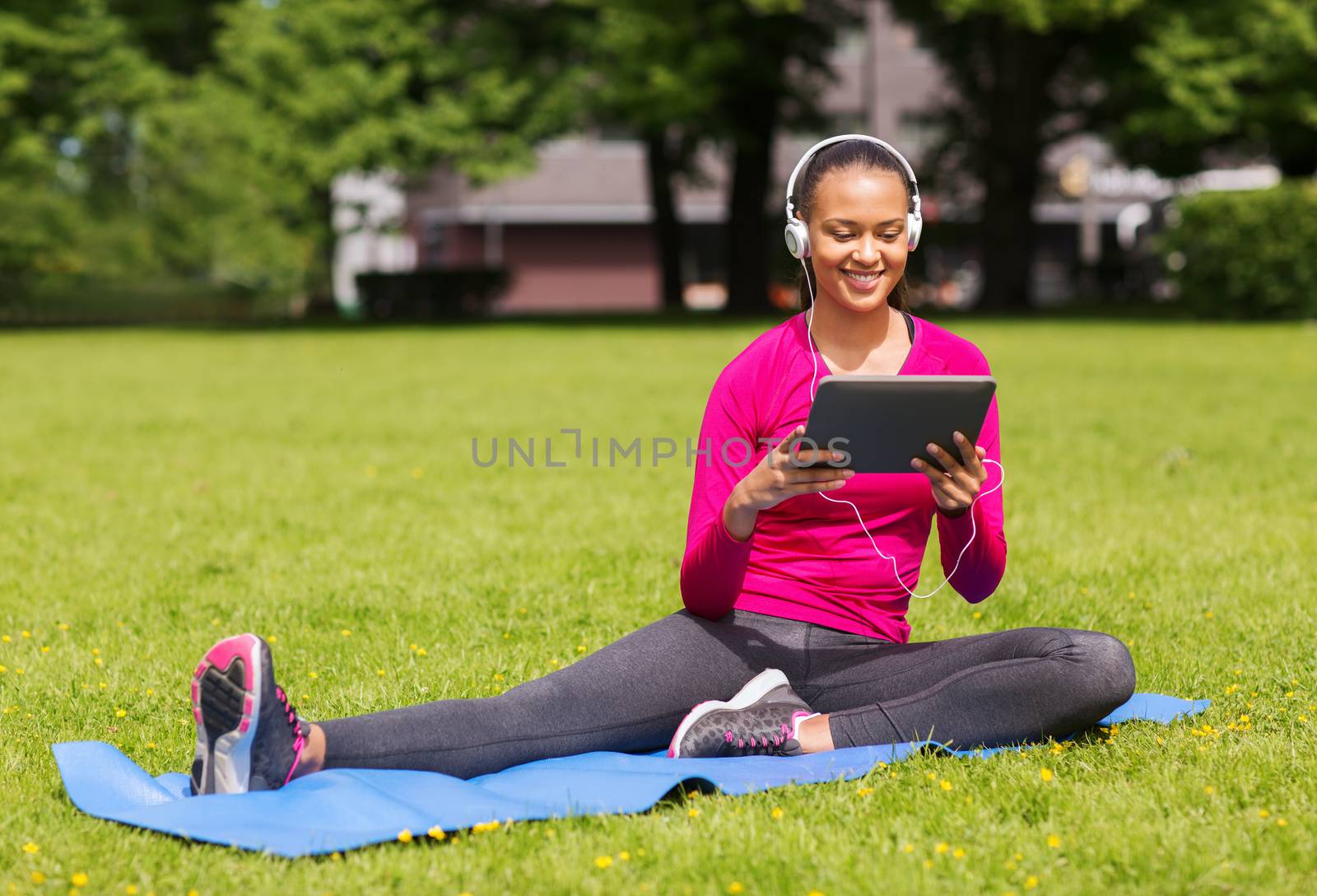 fitness, park, technology and sport concept - smiling african american woman with tablet pc computer and headphones on mat outdoors