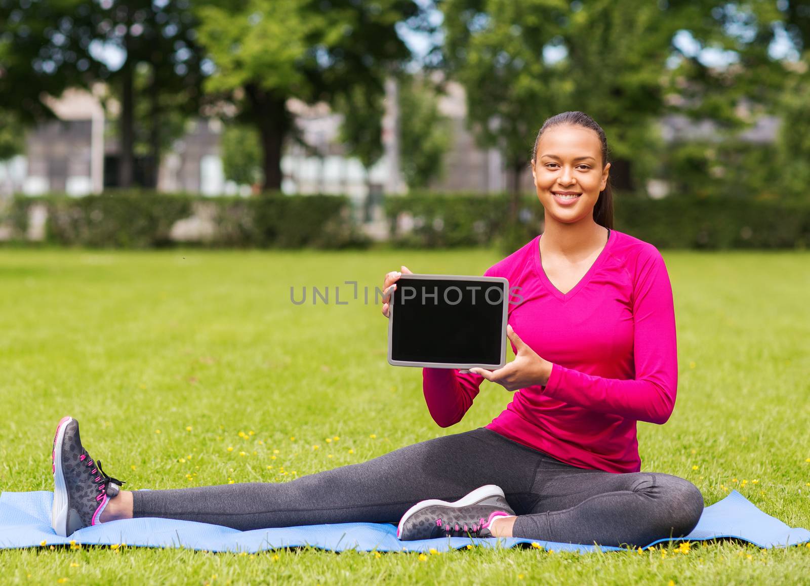 fitness, park, technology and sport concept - smiling african american woman with tablet pc computer sitting on mat outdoors