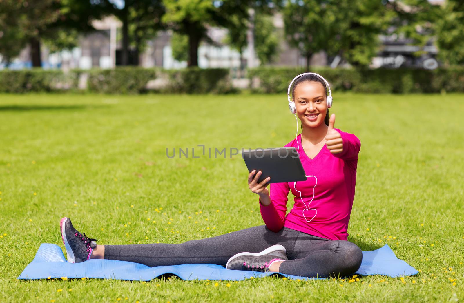 fitness, park, technology and sport concept - smiling african american woman with tablet pc and headphones showing thumbs up outdoors