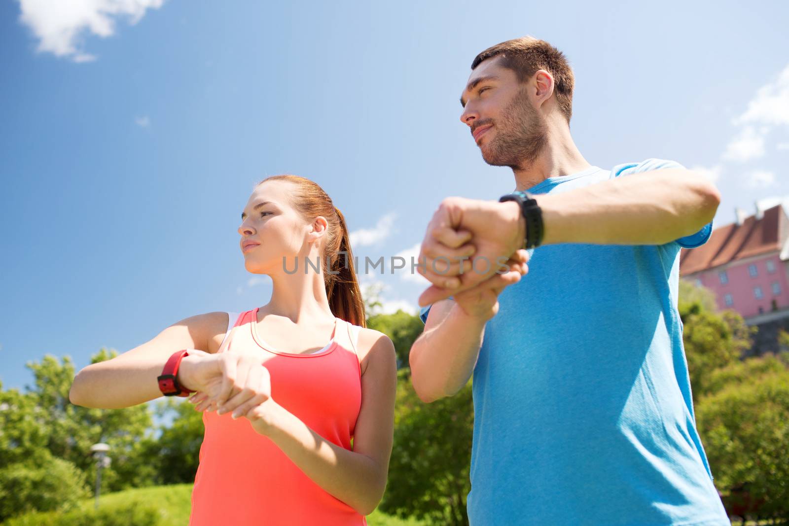 fitness, sport, training, technology and lifestyle concept - two smiling people with heart rate watches outdoors