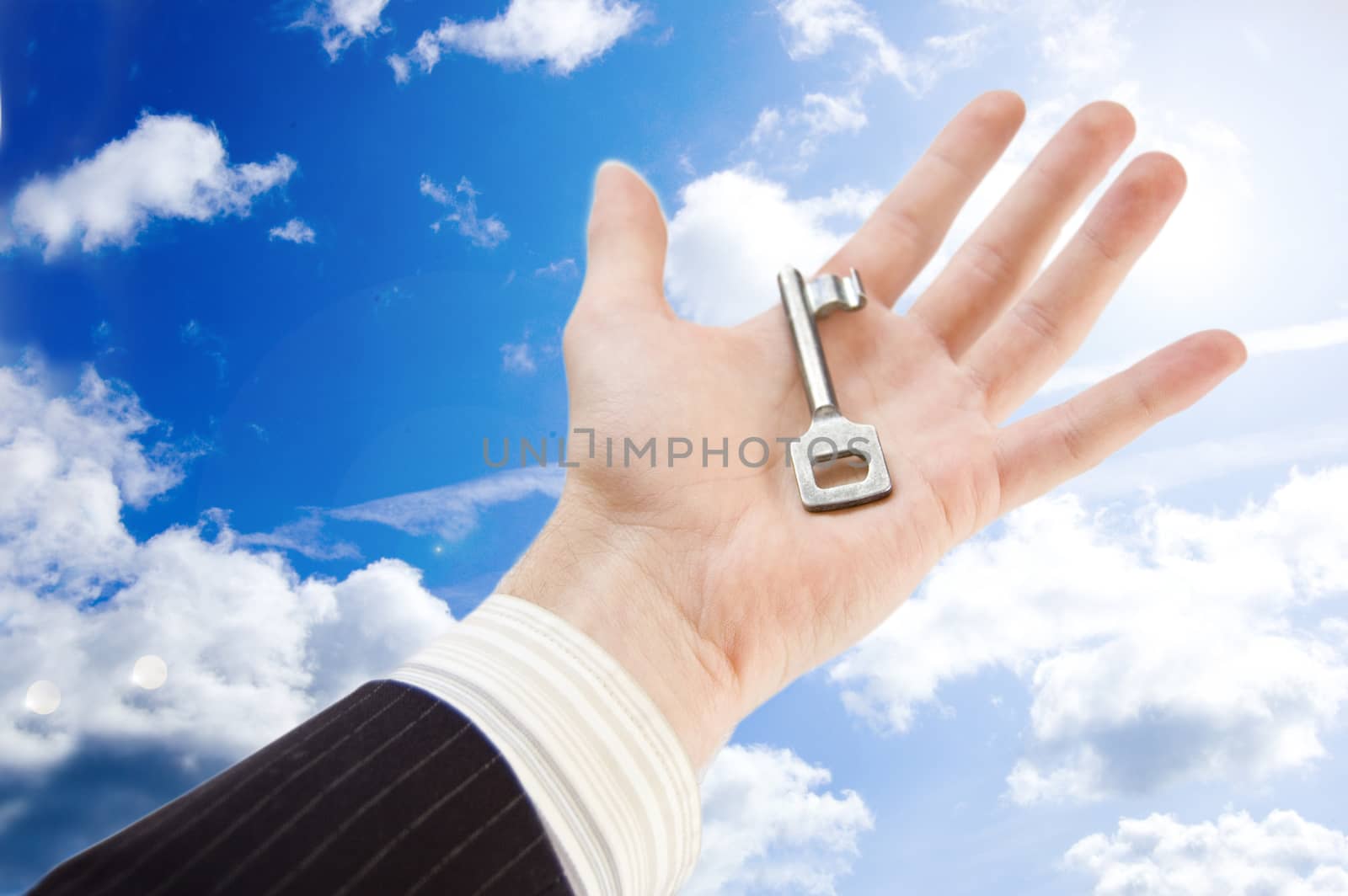 Key to success conceptual image. The businessman holds the key againts the blue sky.