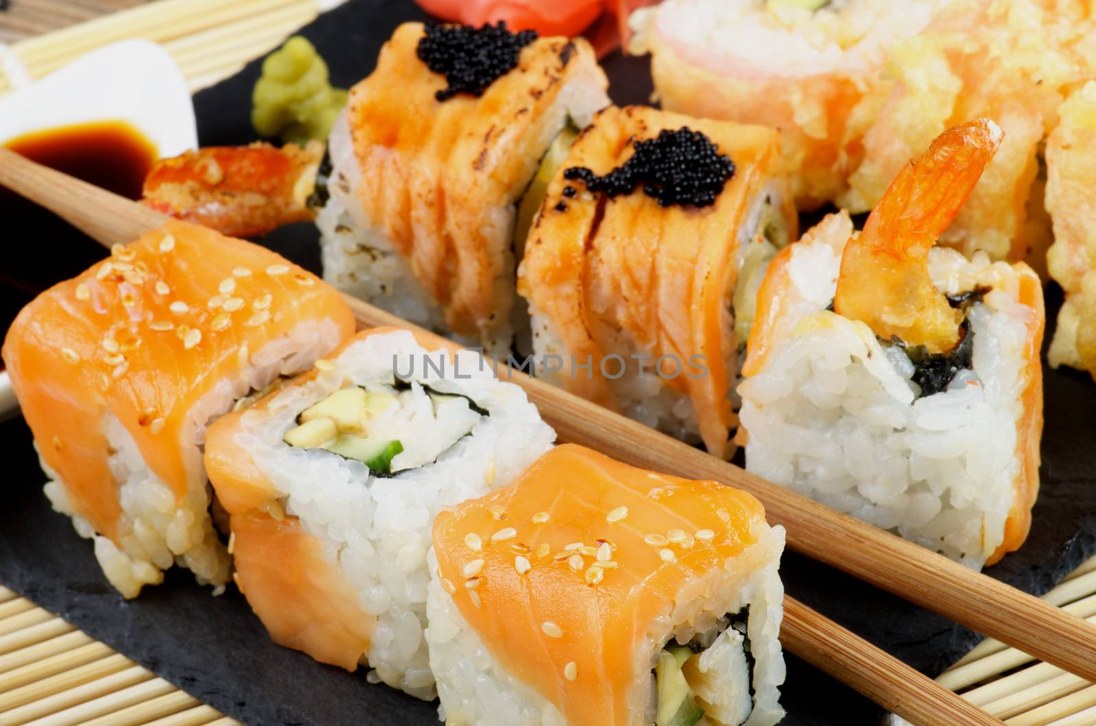 Arrangement of Various Maki Sushi with Smoked Salmon, Eel and Tempura Crab on Stone Plate closeup on Straw Mat background