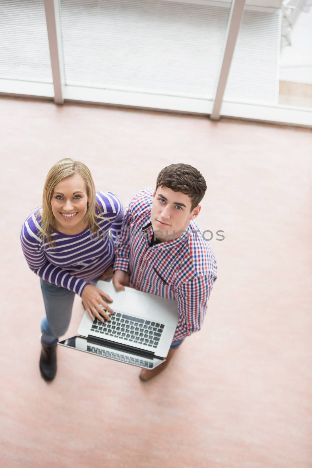 Portrait of happy young students using laptop while standing in college