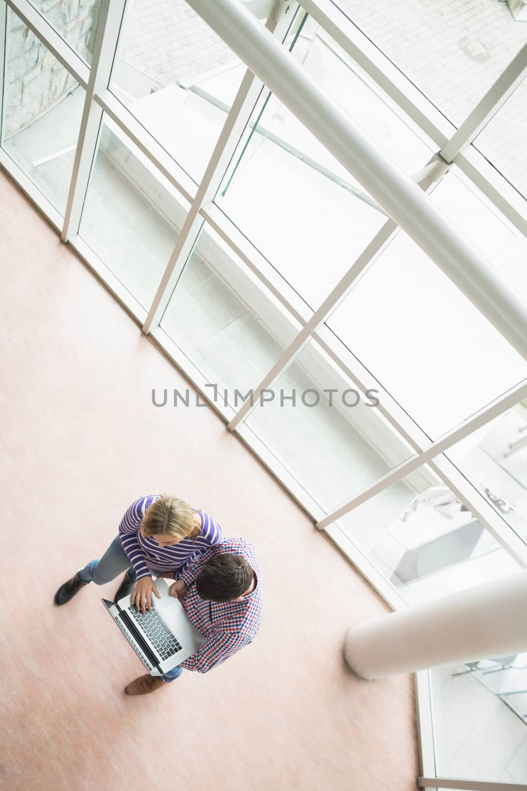 High angle view of college students using laptop while standing by window