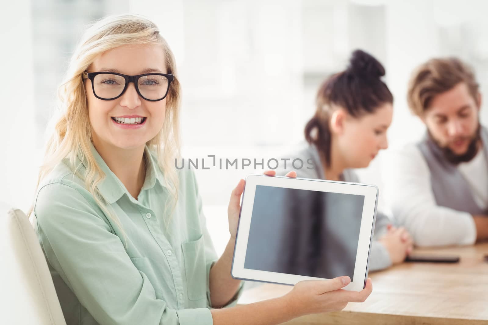 Portrait of smiling woman wearing eyeglasses showing digital tablet at office