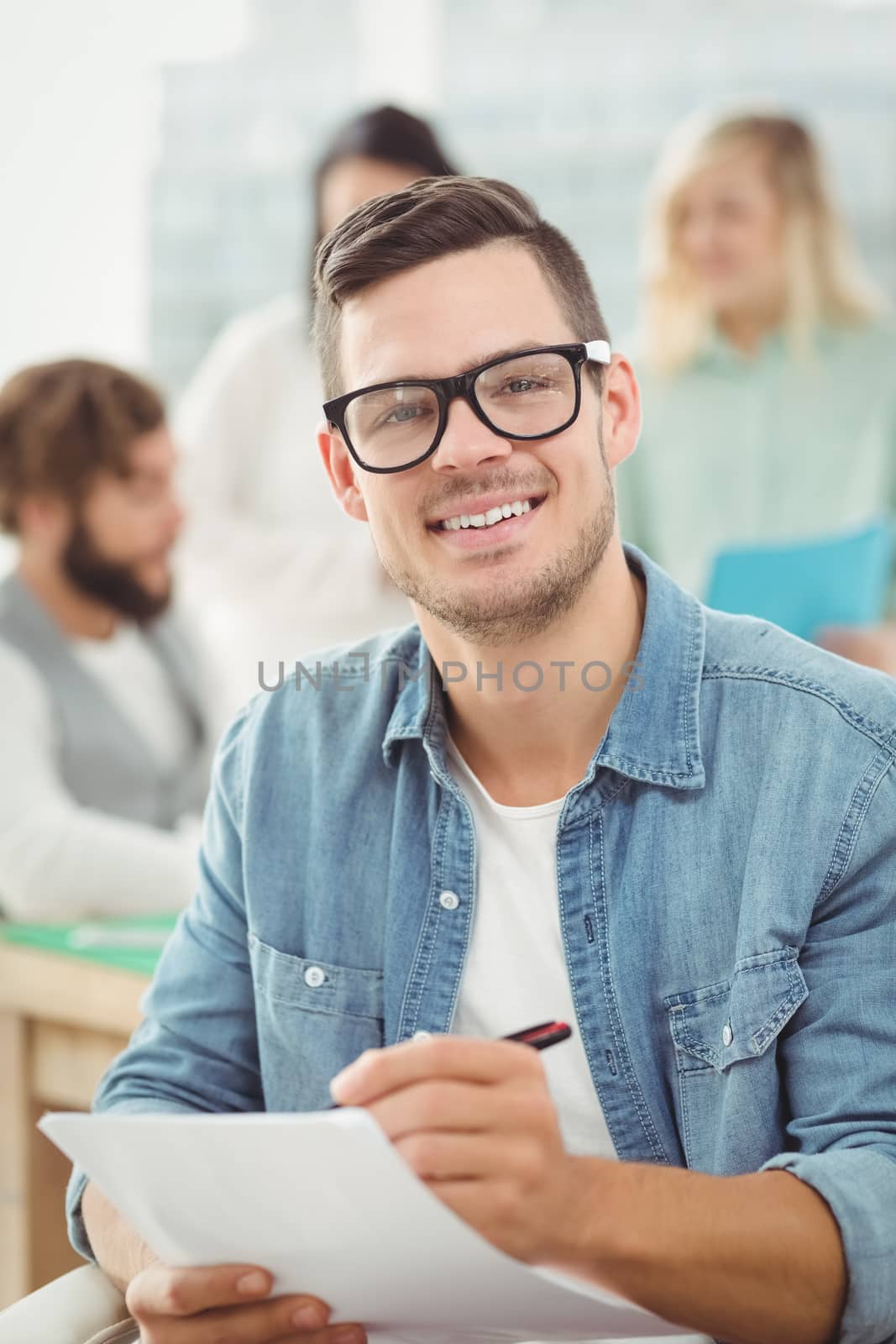 Portrait of smiling man holding paper and pen while working at office
