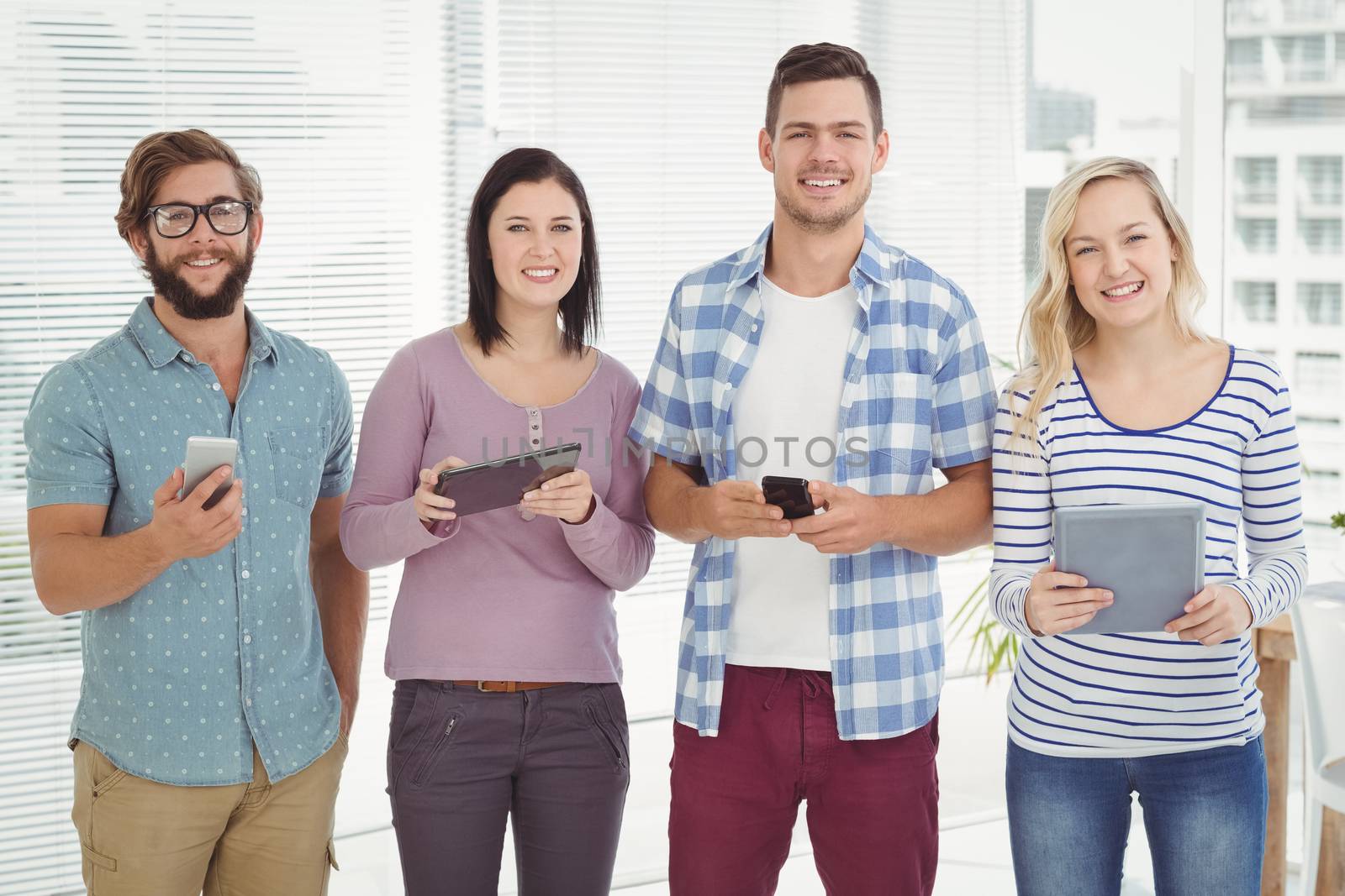 Portrait of smiling business people using electronic gadgets while standing at office