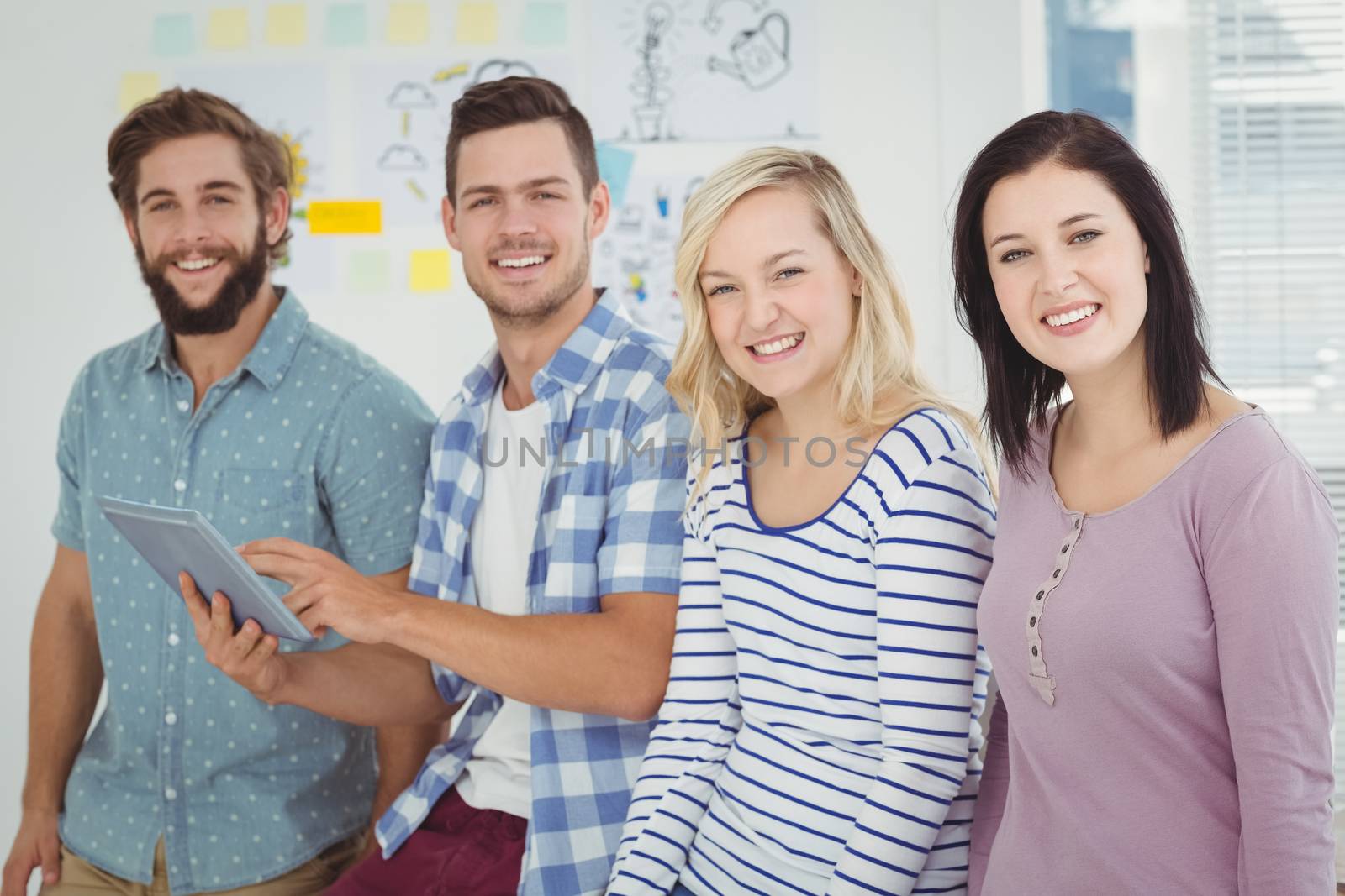 Portrait of smiling man holding digital tablet standing with coworkers at office