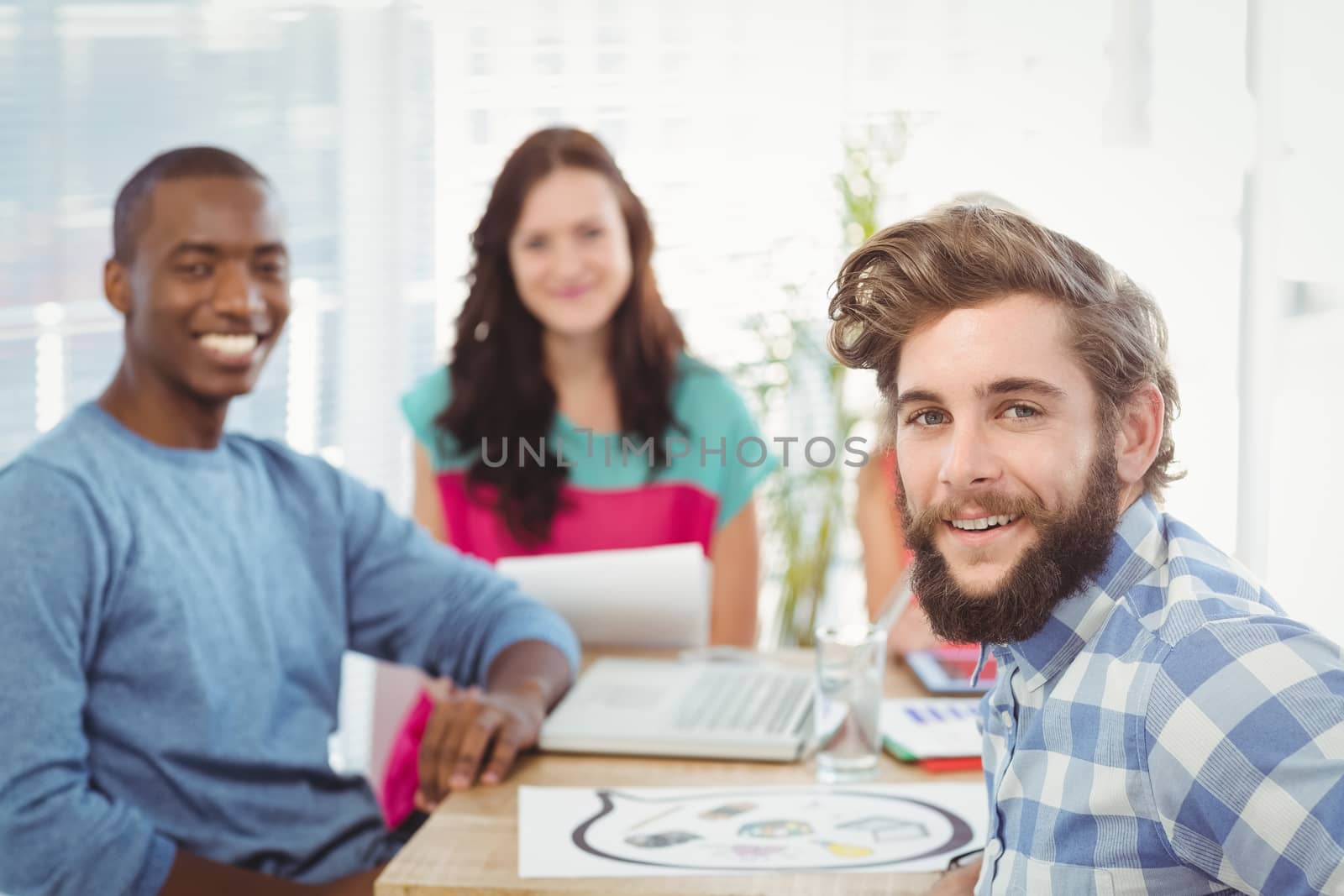 Portrait of smiling business people sitting on chair at desk in creative office