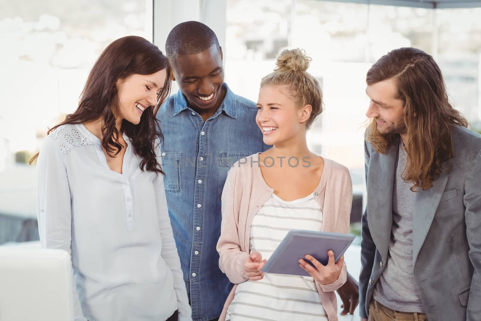 Smiling woman holding digital tablet and discussing with coworkers at office