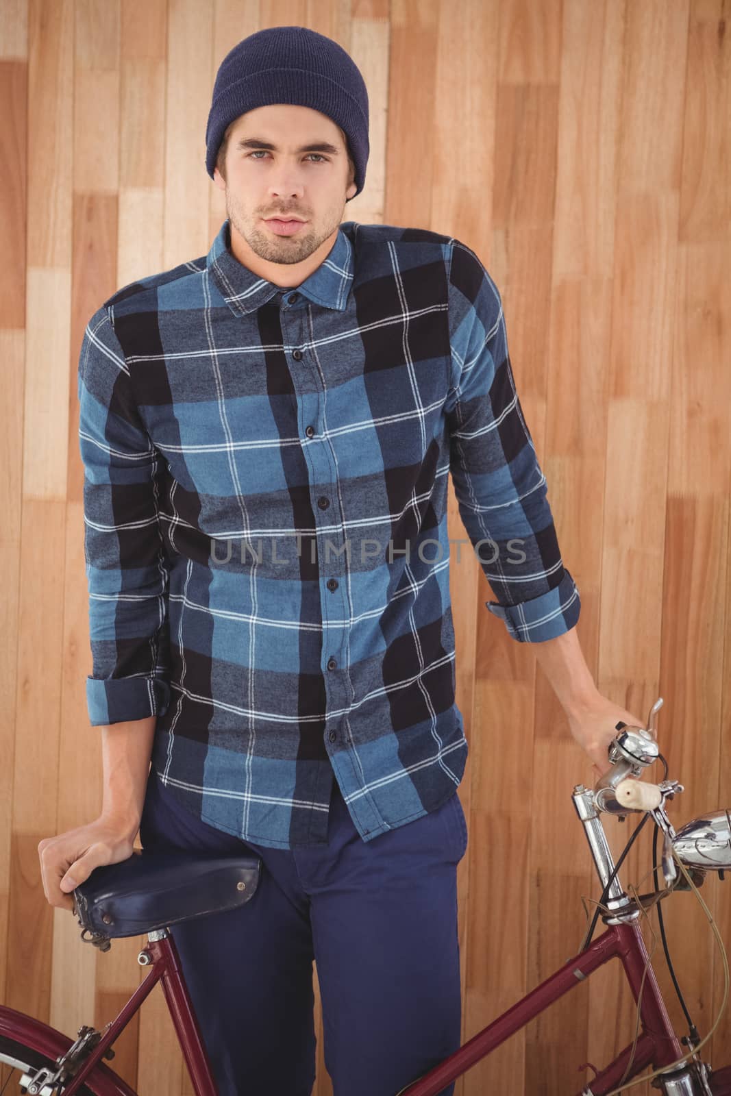 Portrait of hipster standing with bicycle against wooden wall