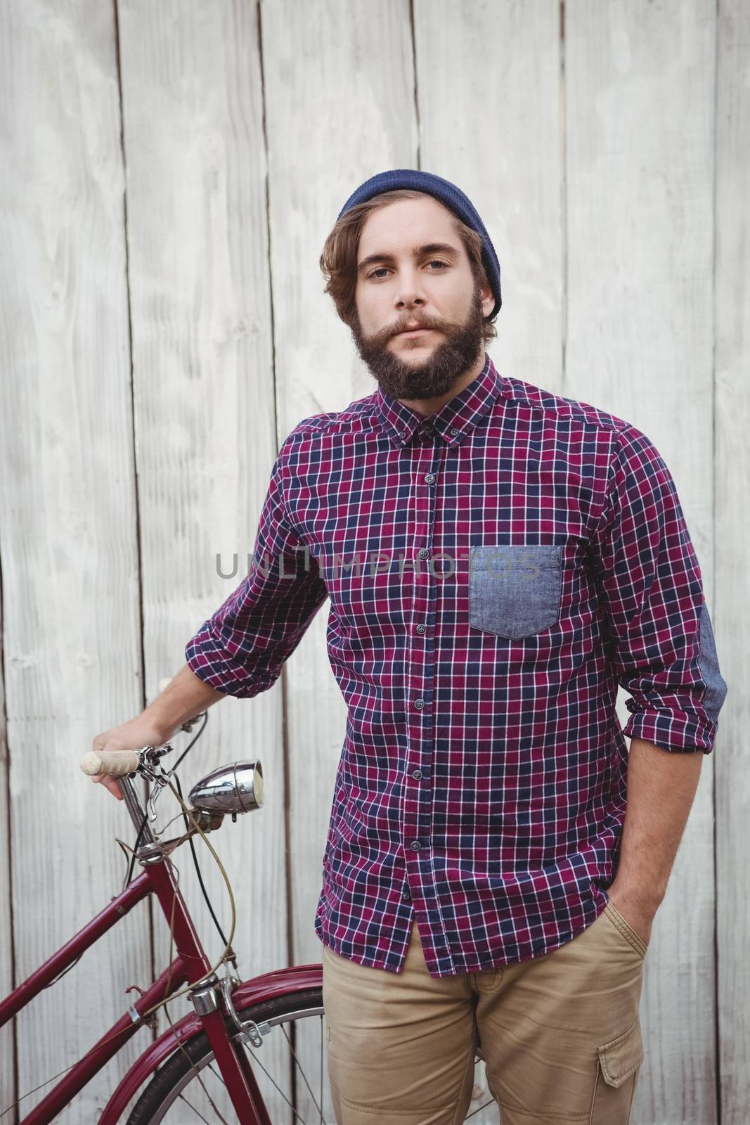 Portrait of confident hipster with bicycle against wooden fence